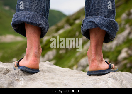 Immagine di panorama che mostra la metà inferiore del mans gambe indossando arrotolato in jeans e flipflops, prendendo da dietro Foto Stock