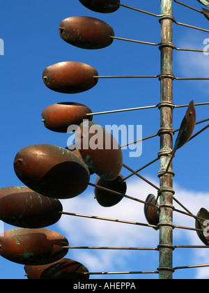 Profondamente colorati in rame o bronzo scultura del vento, il vento ruota, o mulino a vento che si ergono verso l'alto in una spirale contro un nuvoloso cielo blu Foto Stock