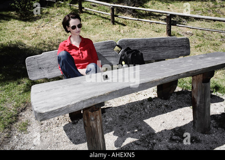 Giovane donna con telefono cellulare seduti sulla panca in legno Dolomiti Alpi europee Italia Foto Stock