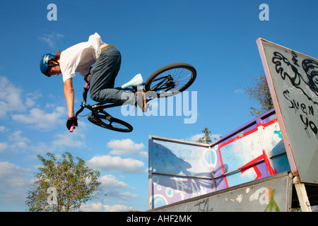 Un giovane ragazzo saltando con la sua moto su un trimestre ad un skatepark Foto Stock