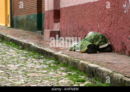 La persona senza dimora di dormire su una strada della Colombia durante una piovosa giornata fredda Foto Stock