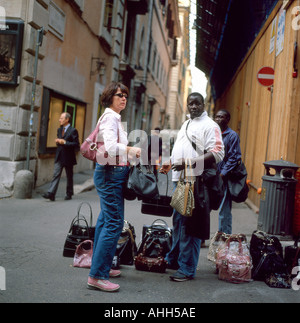 Una donna americana tourist acquisto di merci contraffatte designer borsette da un africano street venditore a Roma Italia KATHY DEWITT Foto Stock