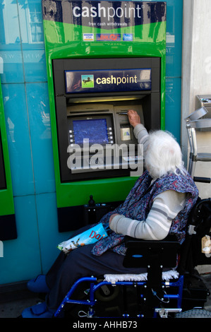 Anziani utenti su sedia a rotelle ritirare contanti da Lloyds Bank bancomat, REGNO UNITO Foto Stock