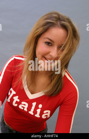 Una splendida bionda ragazza adolescente in una parte superiore rossa con il vento che soffia i suoi capelli attraverso il suo volto Foto Stock