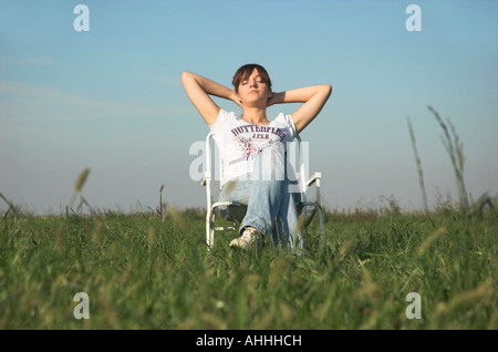 Giovane donna seduta su una sedia in bracci di campo dietro la testa vista frontale Foto Stock