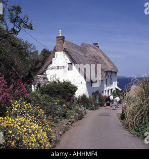 Flowers & tetto di paglia case cottage persone che camminano in stretto Cornish vicolo verso una vista sul mare a Church Cove nella parrocchia di Landewednack Cornwall UK Foto Stock