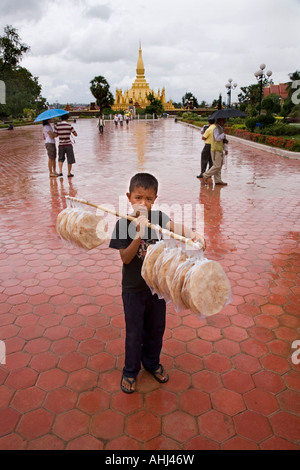 Ragazzo la vendita di pane al Pha That Luang stupa Vientiane Laos Foto Stock