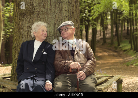 Coppia in pensione seduto sotto un grande albero godendo di uno scherzo Foto Stock