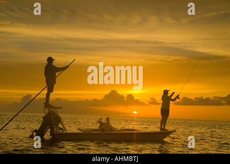 Florida Keys guida di pesca il polling appartamenti barca con donna pescatore colata dalla prua della barca al tramonto nell'oceano dei Caraibi Foto Stock