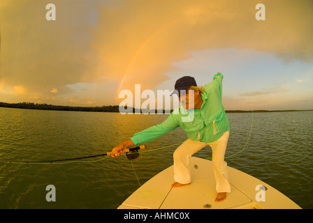 Florida Keys maturo pescatore a mosca la linea di stripping per bonefish sulla prua di una barca di appartamenti a sunrise di arcobaleno in background Foto Stock