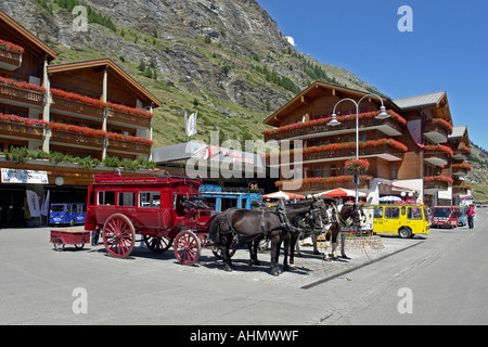 Carrozze trainate da cavalli e veicoli elettrici in attesa per il business nella piazza principale di Zermatt in Svizzera Foto Stock