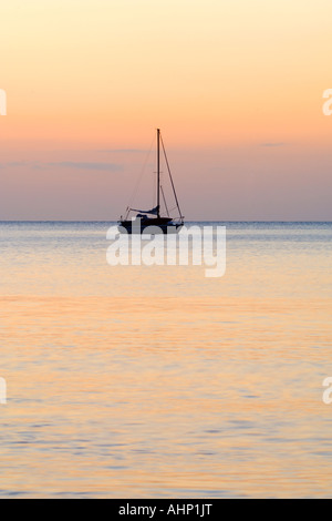 Barca a vela al di ancoraggio su un mare calmo stagliano bagliore arancione del Rising Sun Foto Stock