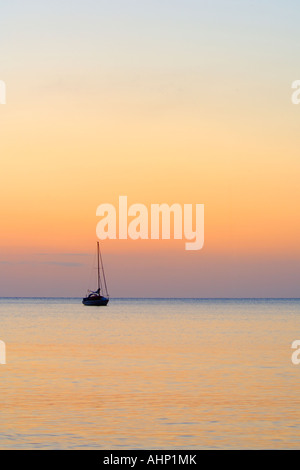 Barca a vela al di ancoraggio su un mare calmo stagliano bagliore arancione del Rising Sun Foto Stock