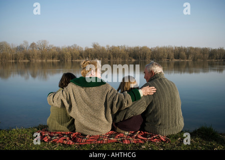 Nonni, nipote (12-14) e nipote (10-12) seduta dal fiume, vista posteriore Foto Stock
