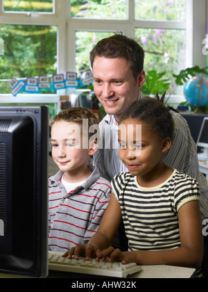 Insegnante maschio guardando il monitor di un computer con un ragazzo e una ragazza Foto Stock