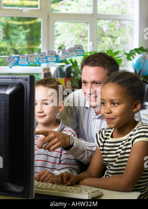 Insegnante maschio guardando il monitor di un computer con un ragazzo e una ragazza Foto Stock