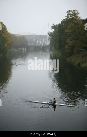 Le donne si appoggia in una roing barca sul fiume Taff a Cardiff, nella distanza il Millennium Stadium può essere visto Foto Stock