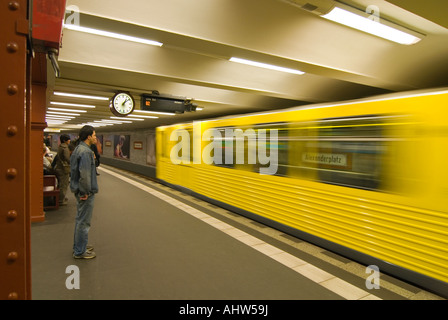 In orizzontale ampia angolazione di persone in attesa sulla piattaforma di Alexanderplatz U-Bahn stazione come un giallo brillante il treno si avvicina. Foto Stock