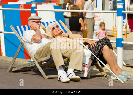 Chiudere orizzontale di pensionati anziani godendo il sole seduti su sedie a sdraio sul lungomare di Weymouth Foto Stock