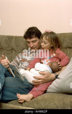 father holding new born son with daughter reading a book Foto Stock