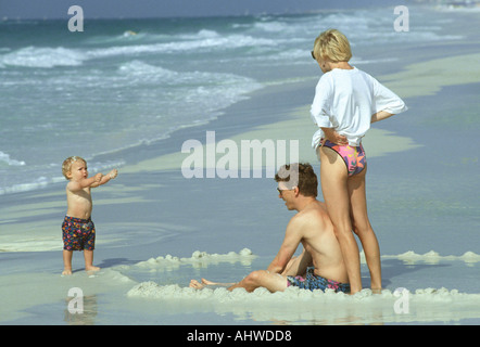 Coppia sposata a giocare con il loro bambino di 18 mesi in spiaggia durante il nuoto Foto Stock