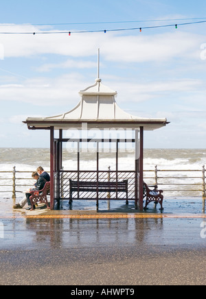 Due persone sat in rifugio in alta marea in una giornata ventosa a Blackpool Foto Stock