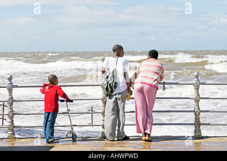 Famiglia di tre persone a guardare il surf in rotolo sul lungomare di Blackpool Foto Stock