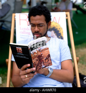 Giovane uomo nero seduto in una sedia a sdraio leggere Joseph Conrad romanzo africano del libro cuore di oscurità al Festival di Hay a Hay su Wye UK KATHY DEWITT Foto Stock