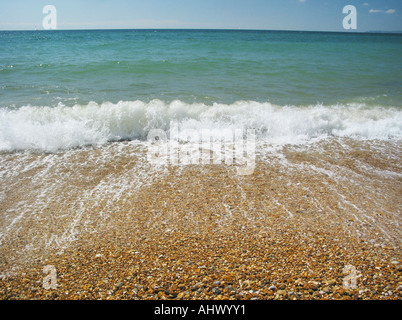 Scena costiere con spiaggia in ciottoli, le onde di laminazione e chiaro cielo blu vicino a Christchurch England Regno Unito Foto Stock