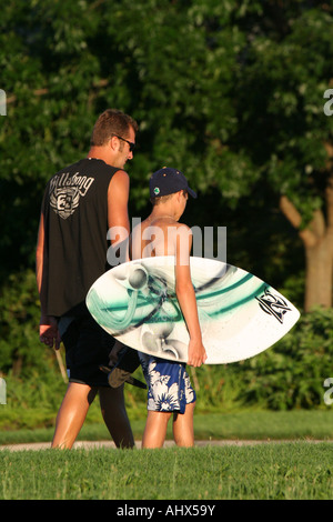 Uomo che cammina con teen che sta portando un skim board Foto Stock