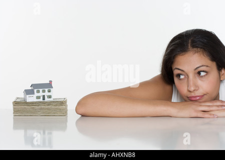 Donna che guarda la casa in miniatura e denaro Foto Stock
