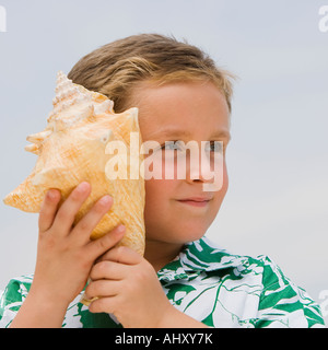 Ragazzo ascoltando conch conchiglia Foto Stock