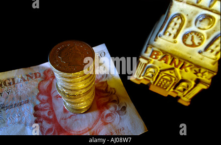 Un mucchio di British pound monete e cinquanta pound note accanto a una banca salvadanaio Foto Stock