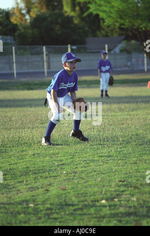 Giovane ragazzo giocando Little League Baseball si erge nel fuori campo lato pronto per qualsiasi hit che può venire il suo modo Foto Stock