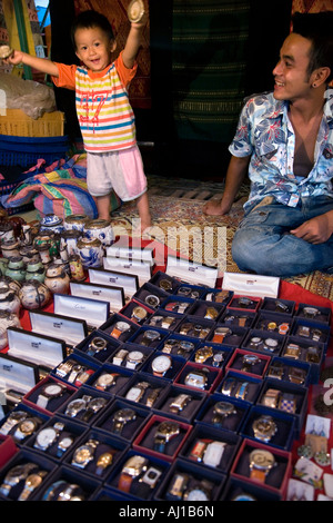 Uomo e suo figlio con prodotti contraffatti, merci contraffatte fanno fuori orologi e penne Mont Blanc. Mercato notturno a Luang Prabang. Laos. Foto Stock