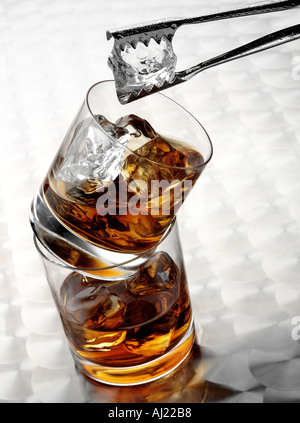WHISKEY IN DUE bicchieri bilanciato sulla parte superiore di ogni altro. Con ghiaccio e pinze Foto Stock