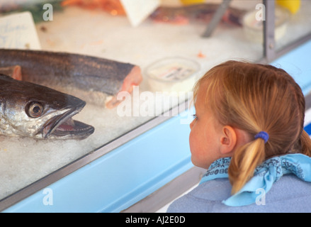 Ragazzina curiosa guardando il grande pesce su ghiaccio in un mercato francese. Foto Stock