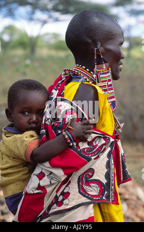 Vista laterale di una donna Maasai in tradizionali abiti colorati e gioielli, portando il suo bambino sulla schiena. Kenya Foto Stock