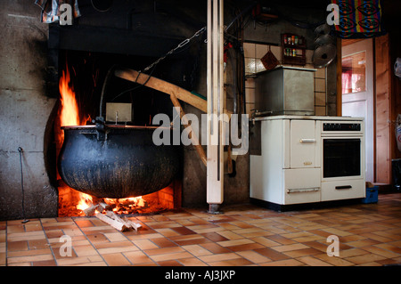 Paiolo di rame pieno di 400 litri di cagliatura del latte il riscaldamento sul fuoco in cucina del chalet di montagna. Foto Stock