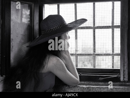 Giovane donna che guarda fuori da una finestra con una grata con la luce del sole proveniente da esso Foto Stock