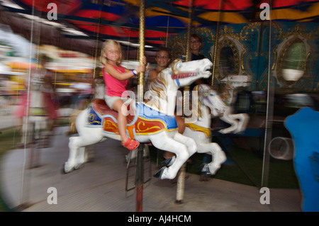 Pan colpo di giovane ragazza sulla giostra con adulti sorridente in background a Harrison County Fair Corydon Indiana Foto Stock