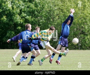 Azione da schoolboy calcio gaelico player calciare il pallone circondato da i giocatori avversari compresi uno immersioni per la sfera Foto Stock