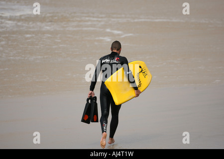 Un corpo Boarder passeggiate lungo una spiaggia portando la sua pensione Foto Stock