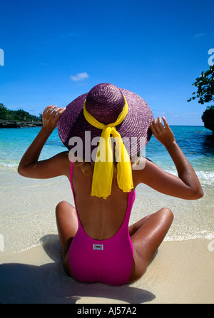 Grand Cayman Sandbar donna in tuta rosa Purple hat siede sulla spiaggia il colpo da dietro Foto Stock