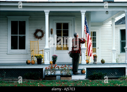 Un orgoglioso senior American uomo appeso una bandiera americana sul portico anteriore della sua antica casa nel Connecticut USA Foto Stock