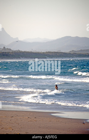 Coppia romantica abbracciando in mare sulla spiaggia di Belongil con montagne in lontananza nella luce della sera Byron Bay New South Wales NSW Aus Foto Stock