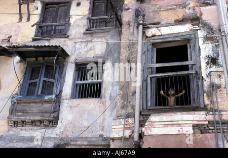 Bambino indiano guardando attraverso barre su una finestra di un edificio fatiscente in Baroda Foto Stock