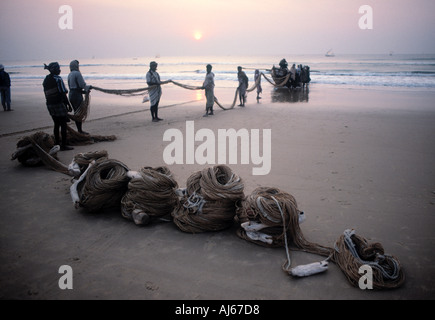 Caricamento dei pescatori le reti sulle loro barche sulla spiaggia all'alba Foto Stock