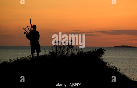 Un bagpiper stagliano contro il tramonto sulla spiaggia Arisaig nelle highlands Foto Stock