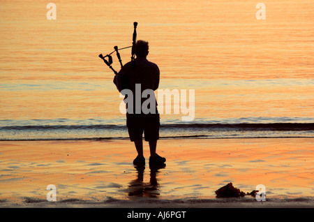 Un bagpiper stagliano contro il tramonto su una spiaggia nelle highlands Foto Stock